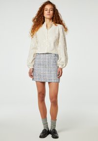 Witte button-up blouse met sterren borduursel; blauw-witte textuur minirok; grijze sokken; zwarte loafers met studs.