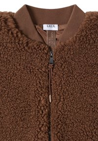 Brown bomber jacket in fluffy texture with knit collar, featuring a front zipper and branding tag on the interior. Lined design with warmth.