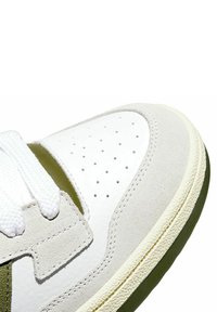 Sneaker in pelle bianca e camoscio grigio con dettagli verdi, dotata di un design perforato sulla punta, lacci bianchi e suola testurizzata.