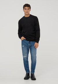 Czarny dzianinowy sweter z okrągłym dekoltem, w połączeniu z dopasowanymi, niebieskimi dżinsami z przetarciami oraz czarnymi botkami za kostkę. Prosty design z minimalnymi akcentami.