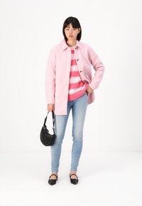 Light pink jacket with buttons, striped pink sweater, blue jeans, black studded handbag, and black flats with decorative details.