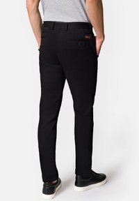 Czarne spodnie w dopasowanym kroju o gładkiej fakturze, z tylnymi kieszeniami i detalem w postaci guzika. W zestawie z czarnymi sneakersami o strukturalnej fakturze.