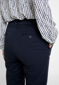 Granatowe spodnie o gładkiej teksturze, z tylnymi kieszeniami i detalem w postaci guzika, zestawione z długim rękawem koszulą w wzory.