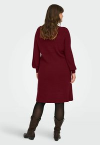 Abito a maglia bordeaux con maniche lunghe e una vestibilità comoda, abbinato a collant neri e stivali alla caviglia marroni. Tessuto morbido, lunghezza al ginocchio.