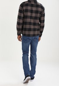 Svart och grå rutiga flanellskjortor med långa ärmar, tillsammans med blå denimjeans och svarta sneakers. Klassisk avslappnad outfits sett bakifrån.