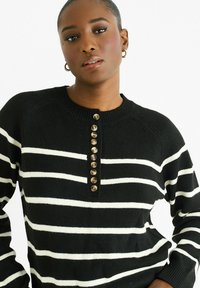 Black and white striped sweater with a crew neck, featuring a button placket and textured knit. Buttons are brown and evenly spaced.