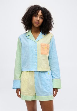 Femme portant un ensemble de pyjama en seersucker multicolore pastel composé d'un haut à manches longues à boutons et d'un short, avec des tons bleus, verts, jaunes et orange.