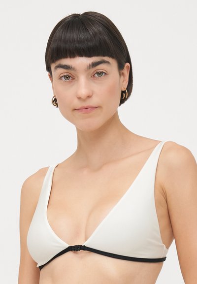 Trīsstūrainais bikini tops baltā audumā ar gludu tekstūru, ar melnu apakškrūšu joslu un centrālo aizdari.