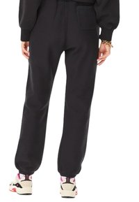 Persona con pantalones jogger negros con puños elásticos y zapatillas blancas con detalles rosas, vista desde atrás.