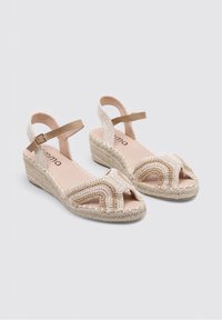 Sandalias de cuña beige con parte superior de tejido trenzado, diseño de punta abierta, tira en el tobillo y suela envuelta en yute, con un patrón de textura trenzada.