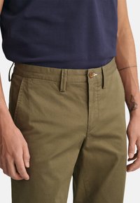 Pantalones de algodón verde oliva con corte ajustado, que cuentan con un cierre de botón y dos bolsillos laterales. Textura suave con sutiles detalles de costura.
