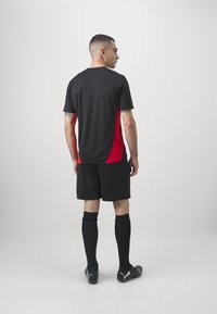 Svart och röd sporttröja med bakdesign, parat med svarta shorts och strumpor. Snyggt, fukttransporterande material. Fotbollsskor.