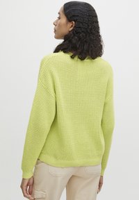 Hellgrüner, gestrickter Pullover mit lockerer Passform. Mit gerippten Bündchen und Saum sowie einem strukturierten Muster. Getragen mit beigen Hosen.