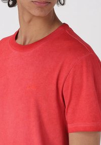 T-shirt in cotone rosso con scollo rotondo e maniche corte. Presenta un ricamo con logo discreto dello stesso colore sul petto.