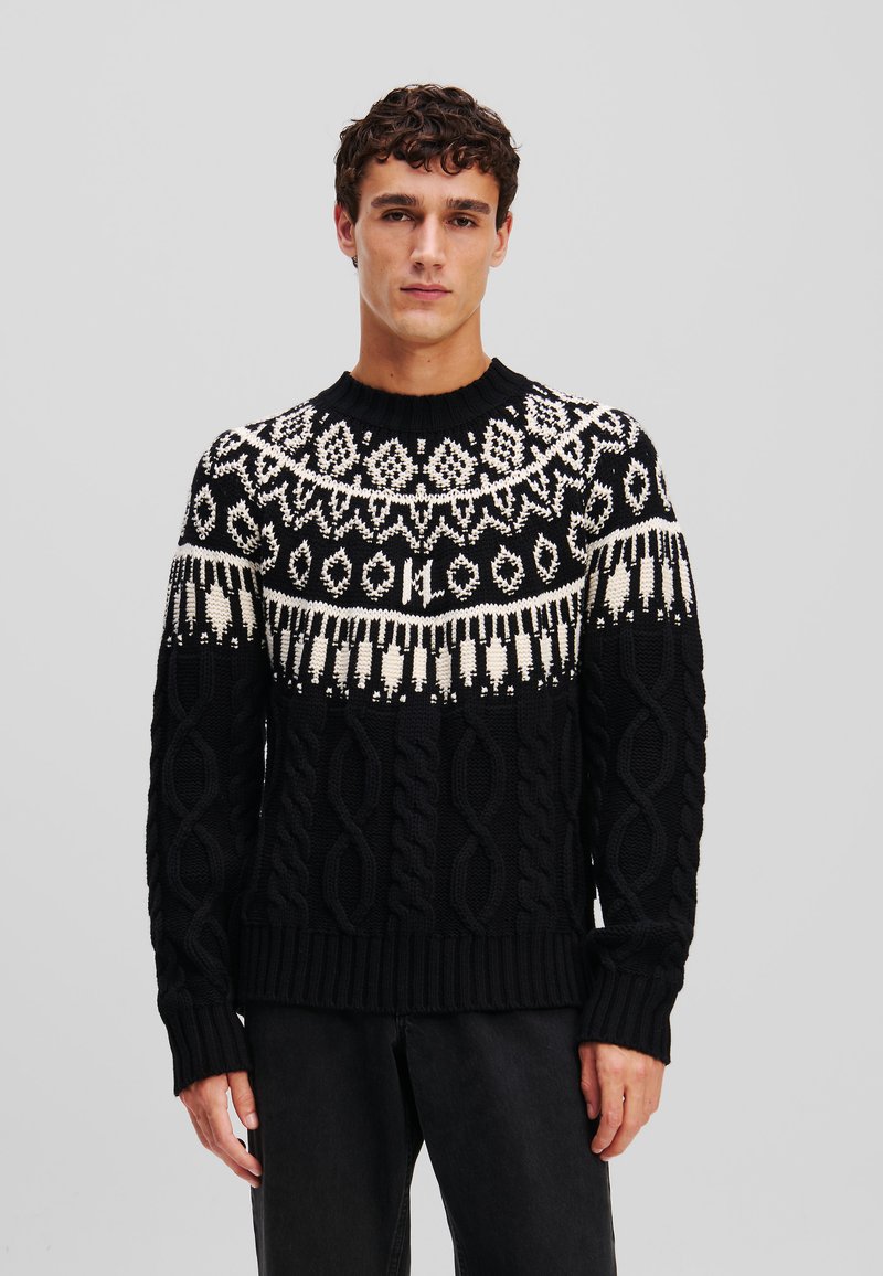 Pull noir avec un motif en tricot torsadé texturé, doté d'une encolure à yoke à motif blanc. Poignets et ourlet côtelés.