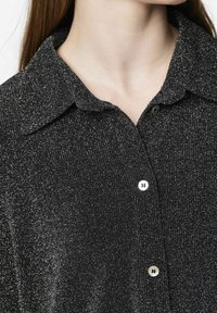 Camicia nera con colletto, caratterizzata da una finitura metallica testurizzata. Presenta riflessi argentati, due bottoni e un scollatura liscia.