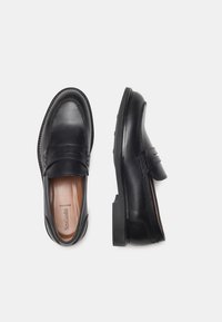 Mocasines de cuero negro con un diseño elegante, que presentan una textura suave, punta redondeada y un sutil acento de costura en el empeine.