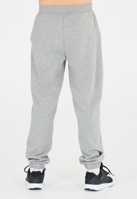 Graue Sweatpants mit einem elastischen Bund und Bündchen an den Knöcheln, kombiniert mit schwarzen Sneakers und weißen Socken. Aus weichem Baumwollmaterial mit einer schlichten Textur.