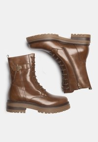Bottes en cuir marron à mi-mollet avec un laçage à l'avant, fermeture éclair sur le côté, semelle texturée et accents métalliques. Finition lisse avec un design robuste.