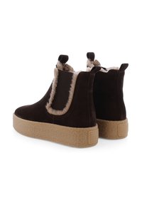 Bruine suède enkelboots met een nep bontafwerking, elastische zijpanelen en een getextureerde tan platformzool. Achteraanzicht toont merkbranding op de zool.