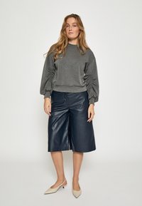 Sudadera gris con mangas fruncidas, combinada con culottes de cuero azul marino de talle alto y tacones nude de puntera afilada.