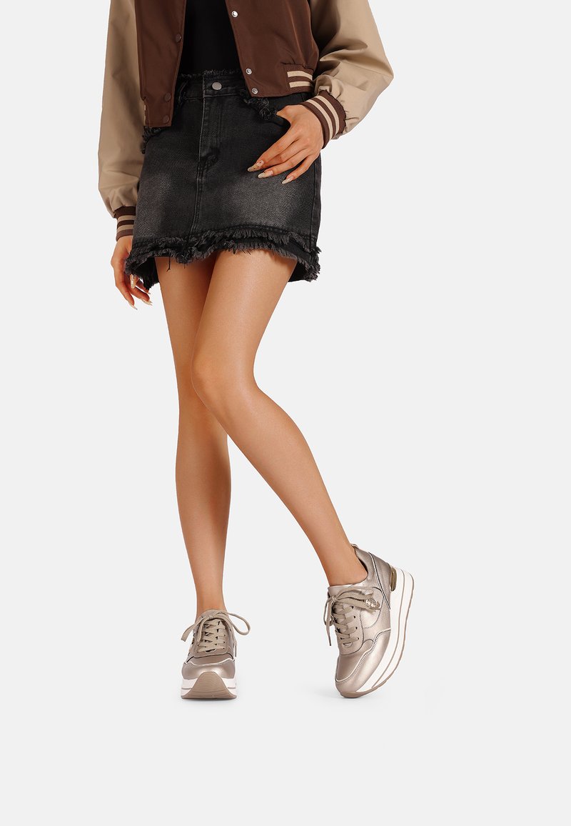 Sneaker in un leggero argento metallizzato con una texture liscia, forma arrotondata e design con lacci. Indossati con una gonna di jeans nera con orlo sfrangiato.