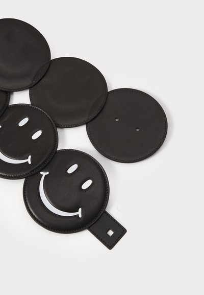 Sottobicchieri in pelle nera con forma rotonda, design di faccina sorridente in bianco embossato e un piccolo manico quadrato su uno di essi.