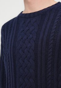 Ζακέτα από σκούρο μπλε πλεκτό ύφασμα με υφή από πλέξη με καλώδια. Διαθέτει στρογγυλή λαιμόκοψη και ριμπ μανσέτες, προσφέροντας άνετη εφαρμογή.