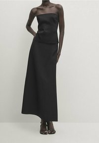Black strapless top paired with a long, flowing black skirt. Smooth, matte fabric with a fitted bodice and a-line silhouette. Open-toe heeled sandals.