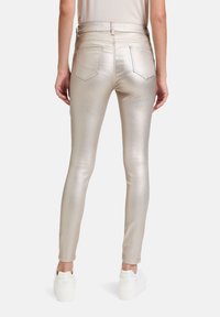 Jeans skinny metálicos dorados con una textura suave, que cuentan con bolsillos traseros, una cintura de subida media y se llevan con zapatillas blancas.