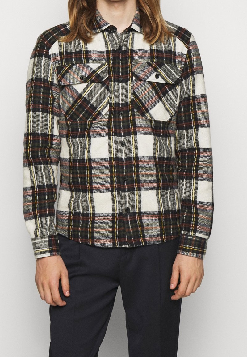 Camicia di flanella a quadri con un mix di motivi bianchi, neri, rossi e gialli, dotata di due tasche sul petto e chiusura con bottoni.