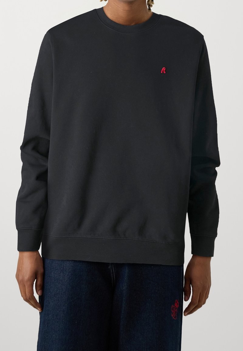 Sudadera negra con cuello redondo, puños y dobladillo acanalados, que presenta un pequeño logo rojo en el lado izquierdo del pecho. Tejido de algodón suave.