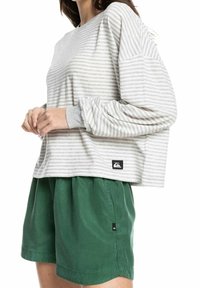 Grau gestreifte Langarmbluse mit lockerer Passform und gerippten Bündchen, kombiniert mit grünen Shorts mit einem seitlichen Logo-Tag.