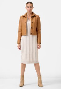Tan læder cropped jakke med krave og fire runde knapper, lagdelt over en beige ribbet strikkjole. Beige ankelstøvler fuldender looket.