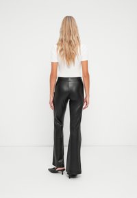Pantalons évasés noirs en simili cuir taille haute avec une texture lisse, associés à une chemise blanche à manches courtes et des mules noires à talons.