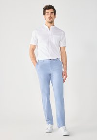Hvit kortermet skjorte med ståkrage og enkelt brystlomme, sammen med lyseblå rettklipte bukser og hvite joggesko.