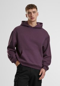 Lila Kapuzen-Sweatshirt aus Baumwollmischgewebe, mit einer Fronttasche und gerippten Bündchen, kombiniert mit schwarzen Hosen.