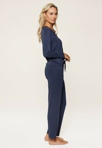Marineblaues Langarm-Pyjama-Set aus weichem Stoff. Das Oberteil hat Spitzenakzente; die Hose hat eine lockere Passform mit einer Kordelzugdetails.