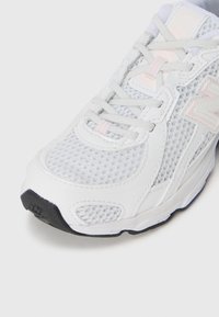 Hvit New Balance løpesko med nettingoverdel, teksturerte detaljer, lyse rosa aksenter og svart gummisåle.