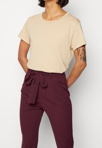Beige T-Shirt mit kurzen Ärmeln und runder Ausschnitt, kombiniert mit tief burgunderfarbenen, hoch taillierten Hosen mit einer vorderen Schleife und weitem Bein.