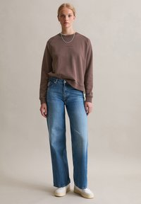 Felpa marrone con scollo rotondo, abbinata a jeans a gamba dritta blu a vita alta e sneaker bianche. Collana in argento semplice.