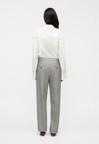 Λευκό πουκάμισο με μακριά μανίκια και λεπτομέρεια ραφής στην πλάτη, συνδυασμένο με ανοιχτό γκρι ψηλόμεσο παντελόνι με δύο πίσω τσέπες και πιέτες.