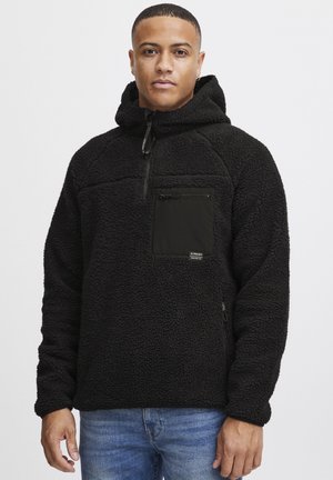 Black fleece pullover with a zippered chest pocket, textured surface, and adjustable hood. Features side zipper and contrasting fabric accents.