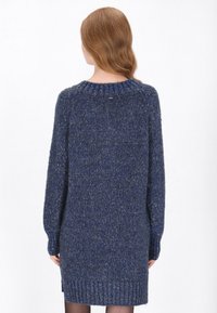 Sötétkék kötött pulóverruha texturált felülettel, bordás szegéllyel és hosszú ujjal. Magas nyakkivágással és diszkrét fényzéssel rendelkezik.