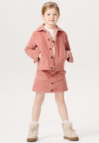 Lyserød cordjakke med knaplukning, parret med en matchende nederdel, begge med lodrette striber og en blød tekstur. Beige snørebåndsstøvler.