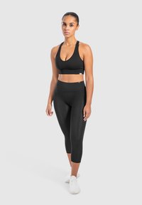 Reggiseno sportivo nero e leggings a vita alta, con una texture liscia e un design aderente. Le scarpe sono bianche con dettagli discreti.