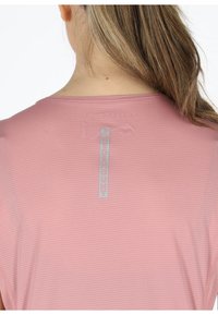 Pink short-sleeve top with a textured fabric, features a logo tag vertically aligned at the back neck, and smooth seams.
