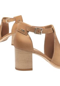 Sandali con tacco color sabbia, punta chiusa, lati aperti e cinturino alla caviglia. Presentano materiali lisci e testurizzati; tacco a blocco impilato con effetto legno.