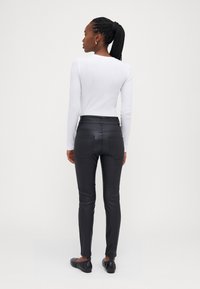 Witte langemouwen top, aansluitend, gecombineerd met hoge taille zwarte broek. Glad textuur met achterzakken en enkel-lange ontwerp. Zwarte schoenen.
