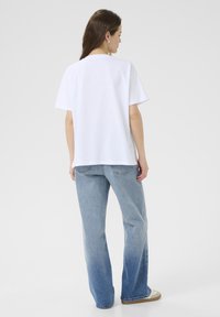 White cotton T-shirt with short sleeves, round neckline, and relaxed fit, paired with light blue denim jeans featuring slight fading.